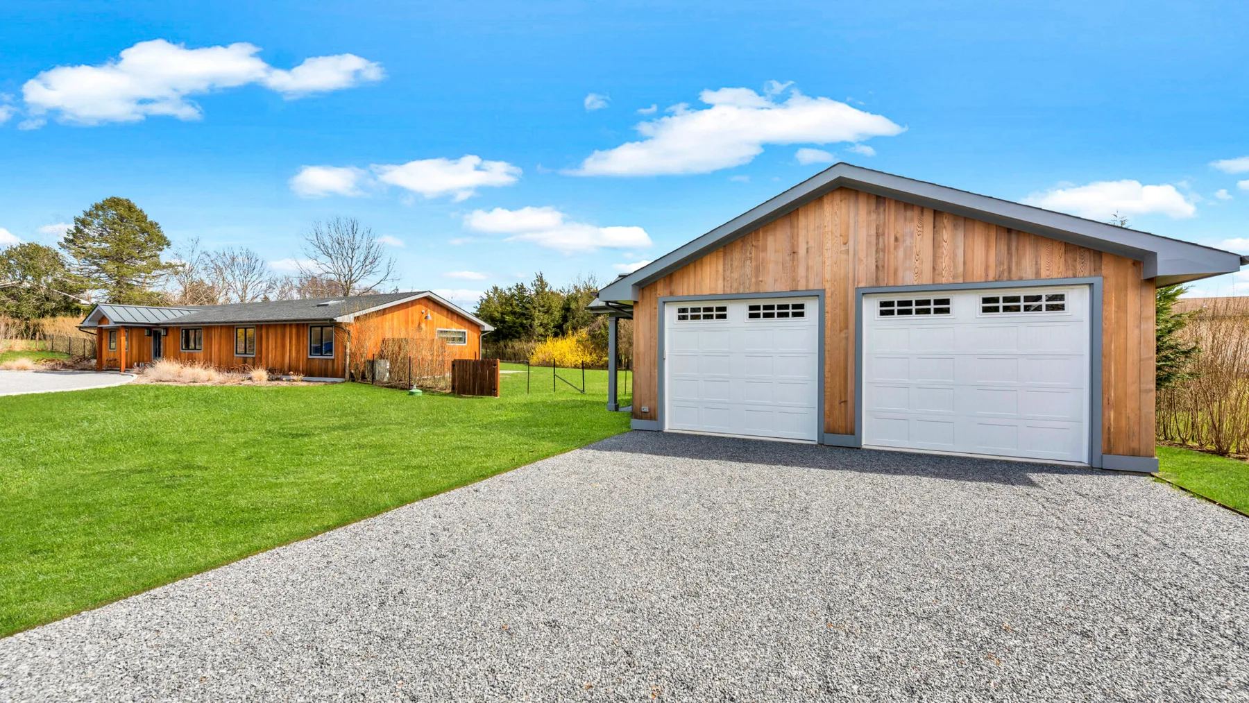 A detached garage with two doors stands beside a broad gravel driveway and green lawn.