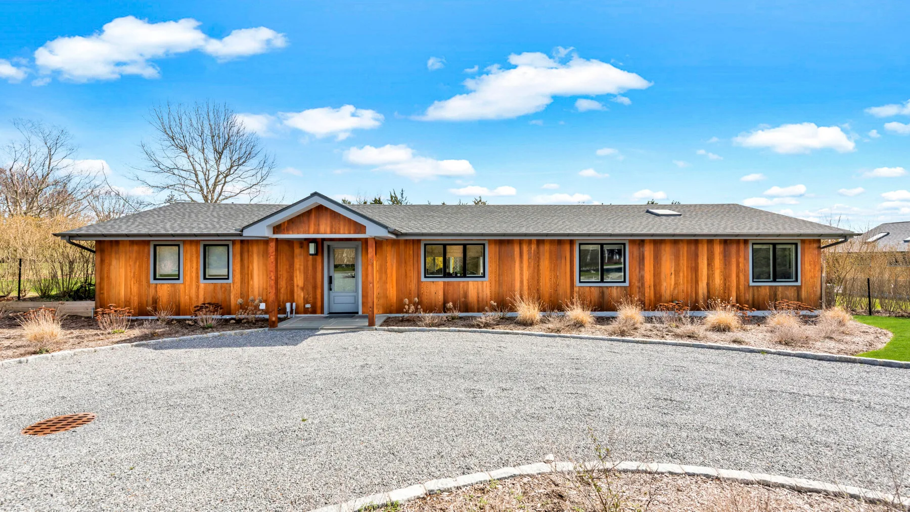 A long, single-story house faces a broad gravel driveway.