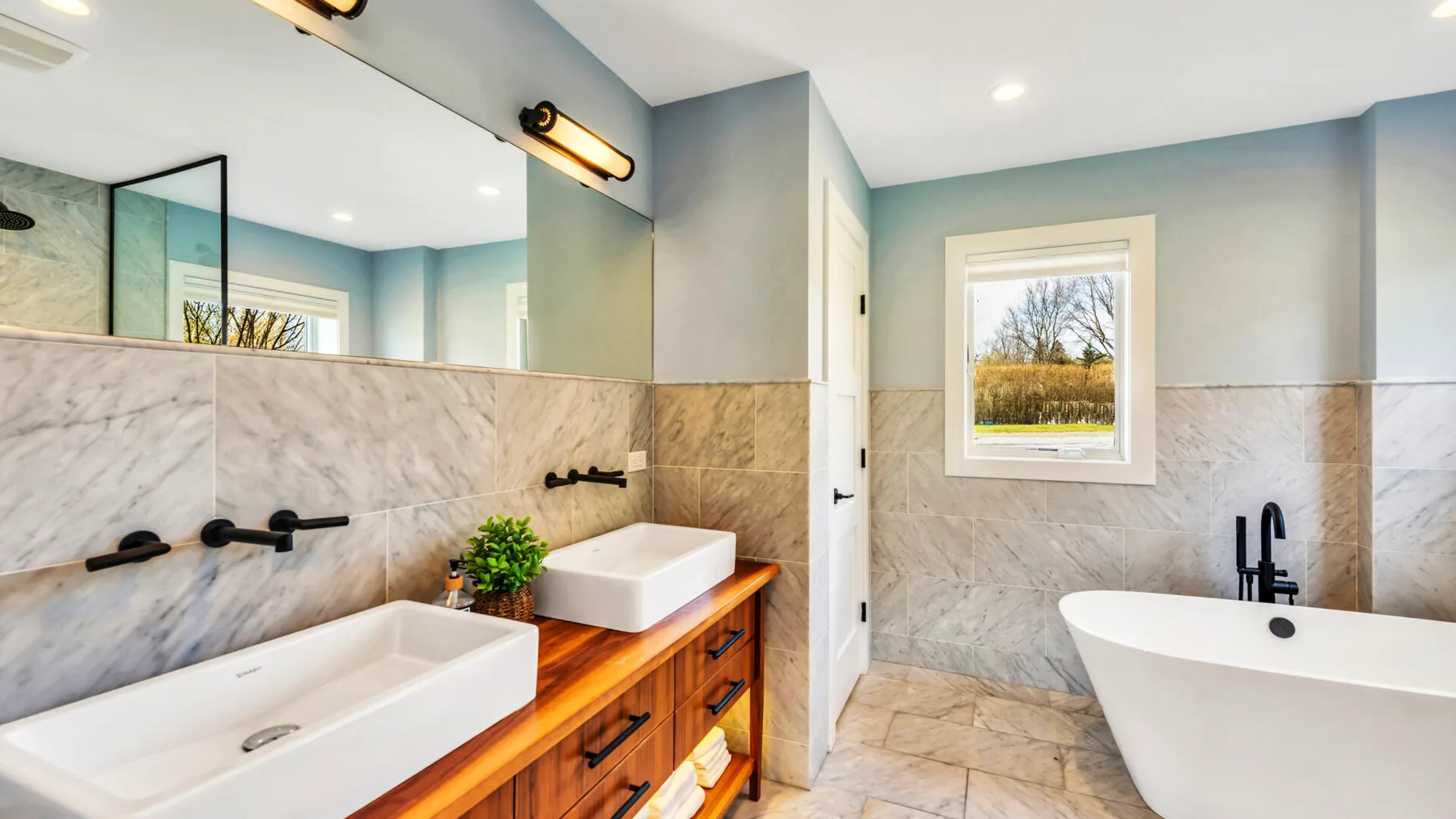 A bathroom with a long vanity and a freestanding bathtub beneath a window.