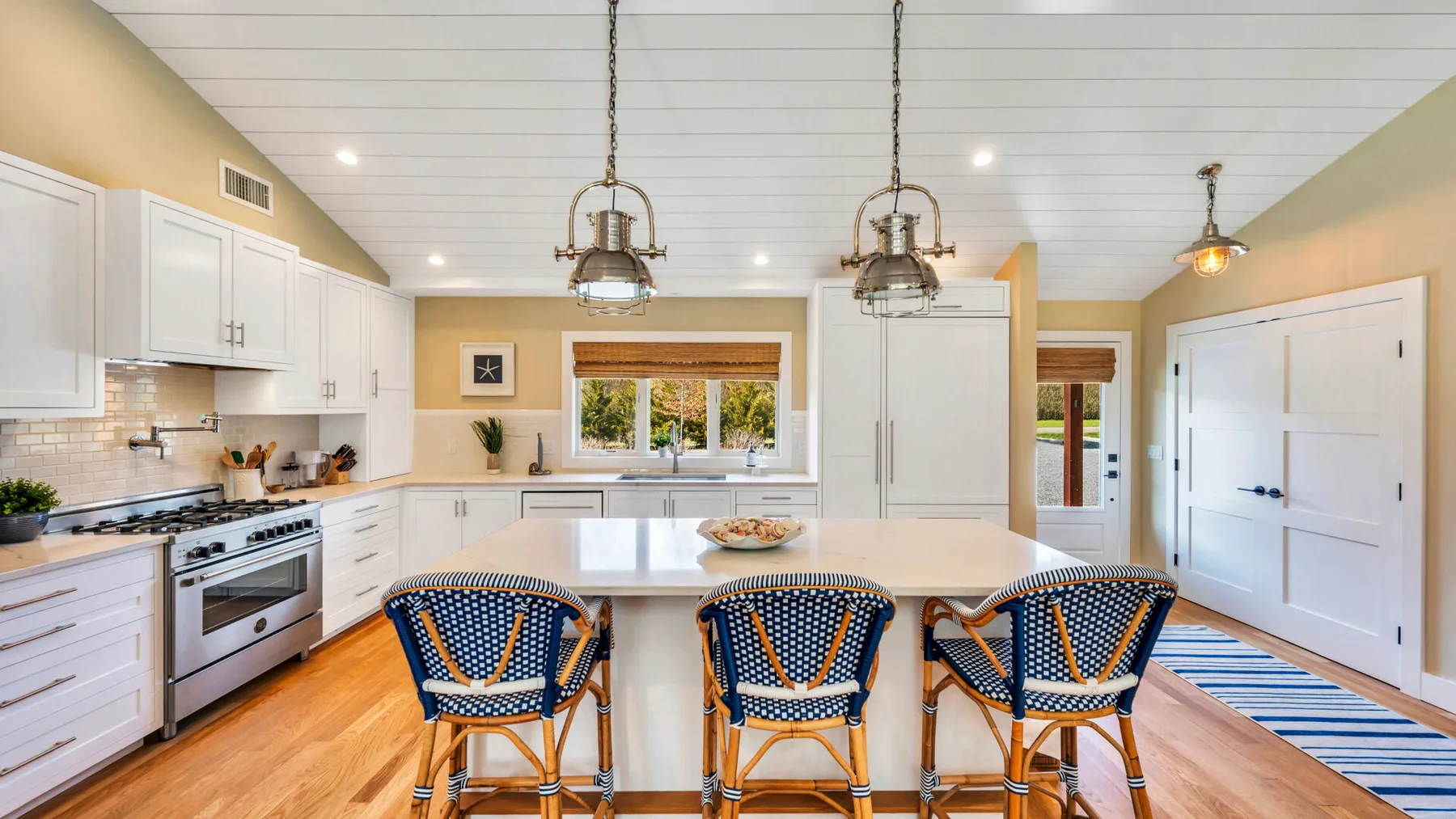 A bright kitchen with a central island and blue woven seating.
