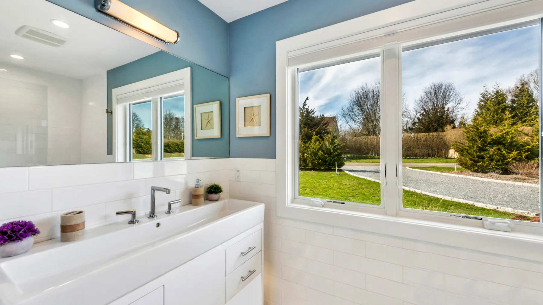 A bright bathroom vanity sits beside a large window overlooking a green lawn.