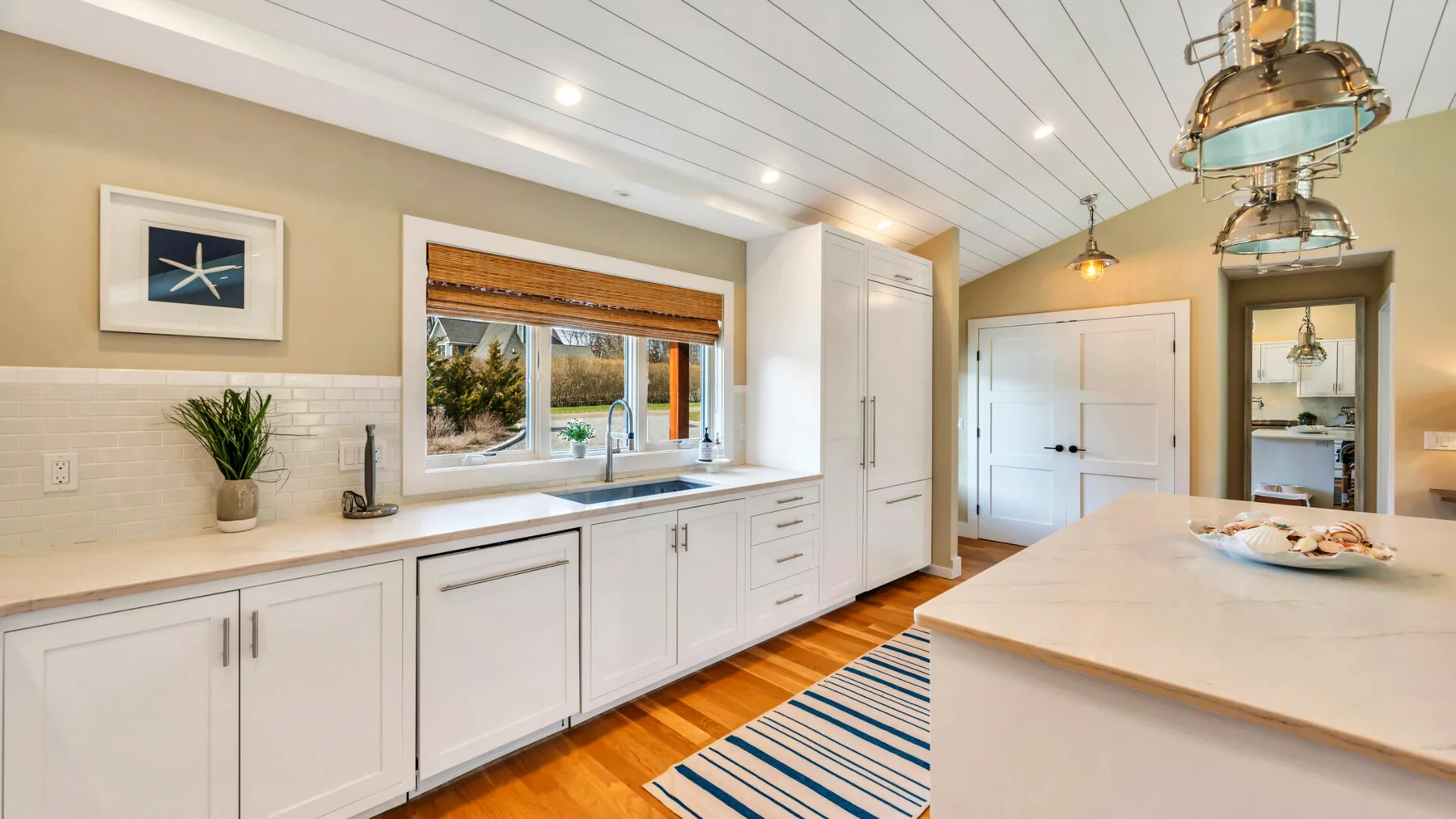A bright kitchen with white cabinetry, a large island, and striped floor runner.