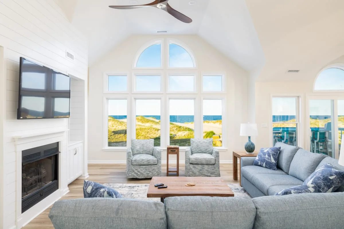 Una sala luminosa con asientos, chimenea y grandes ventanas con vistas a la playa.