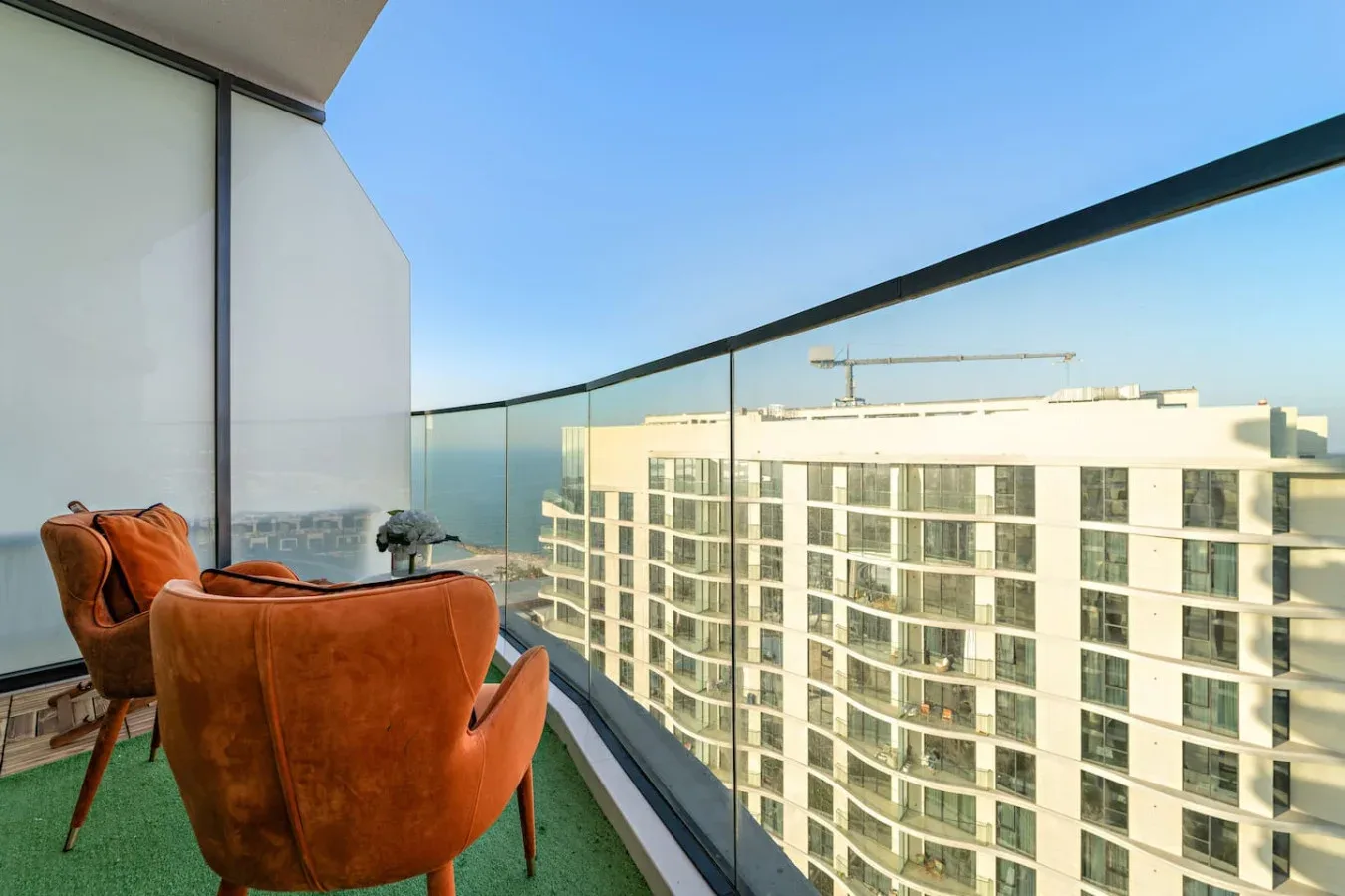 A balcony with orange seating overlooks a neighboring building and the water.