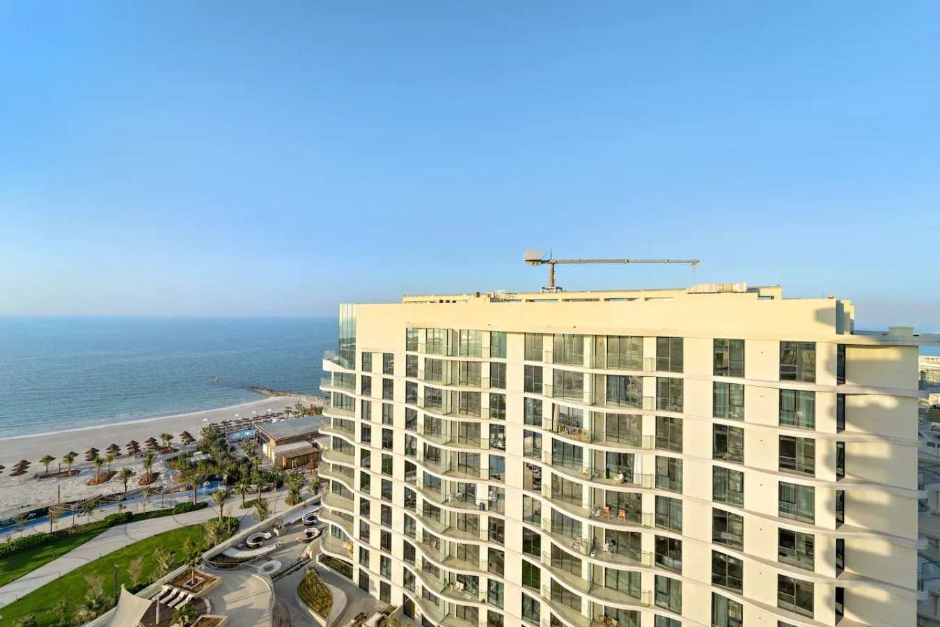 Coastal high-rise building beside the sea, with a landscaped shoreline in view.
