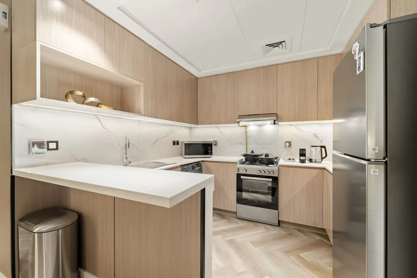 A compact kitchen with light wood cabinetry, a white countertop, and stainless-steel appliances.