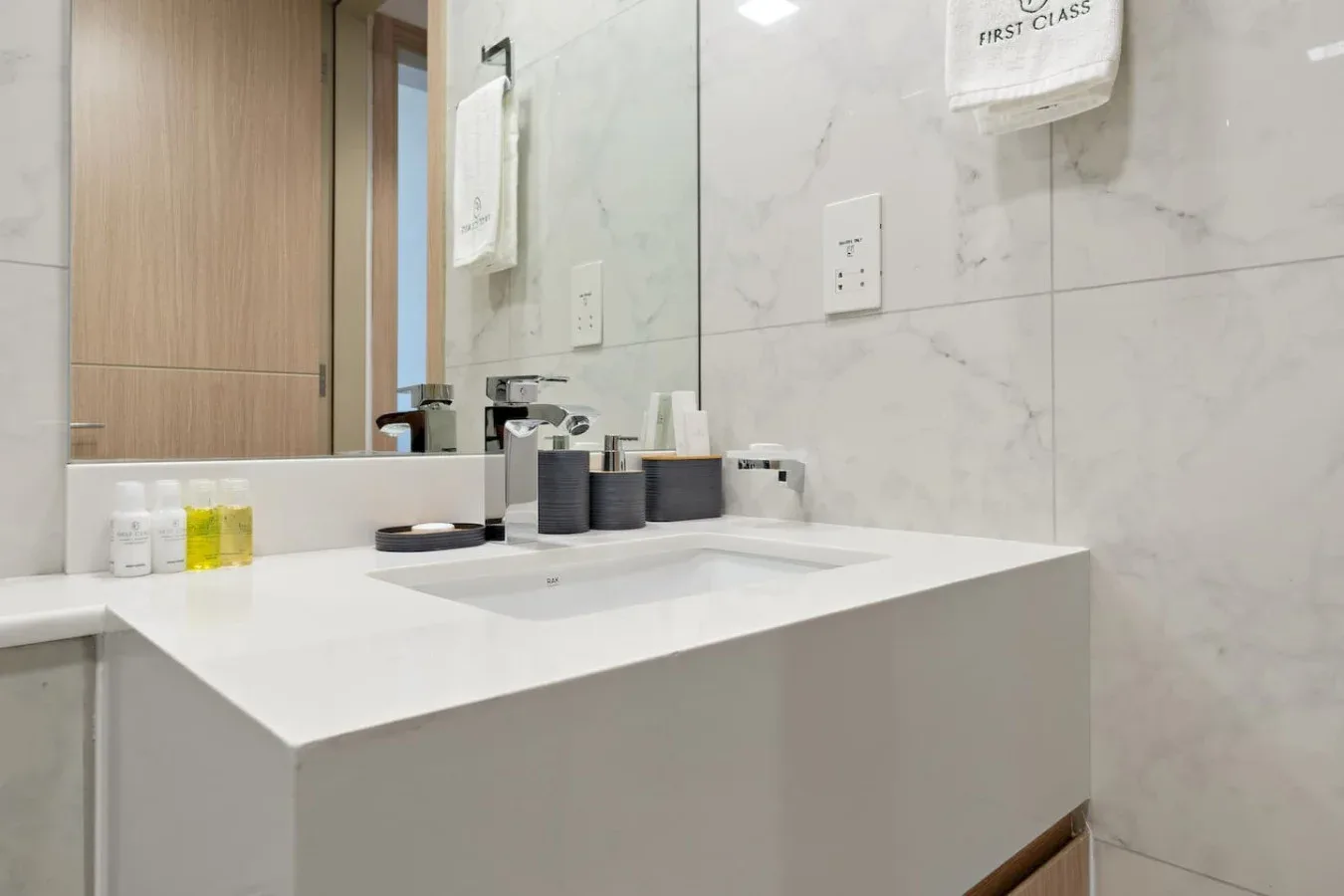 A modern bathroom vanity with a wide white countertop and toiletries.