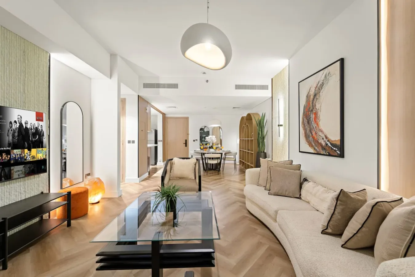 A bright living room with a seating area, glass coffee table, and large wall artwork.