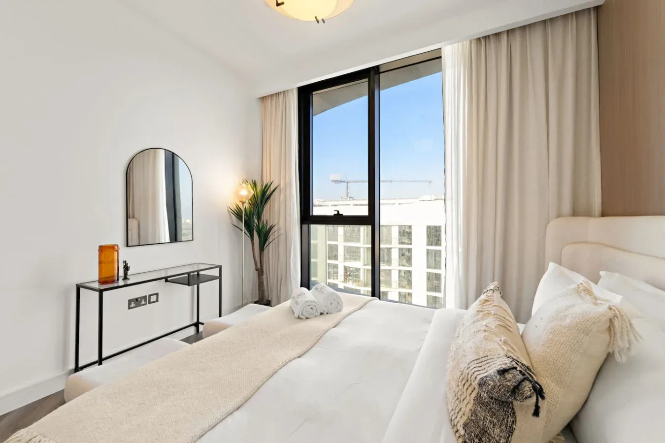 A bright bedroom with a bed, neutral bedding, and a large window.