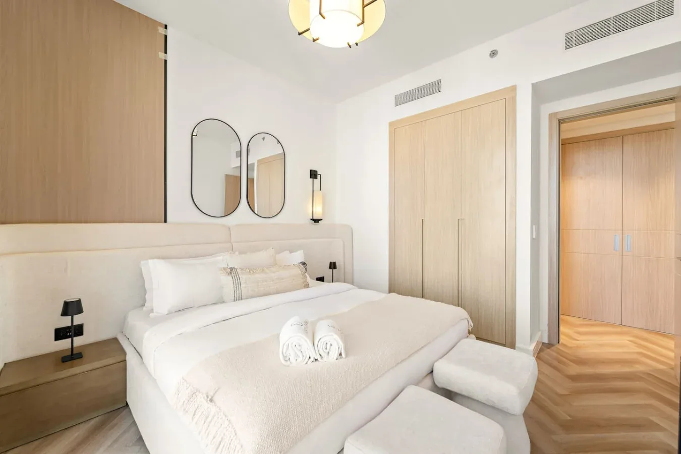 A bright bedroom with a neatly made bed and light wood cabinetry.