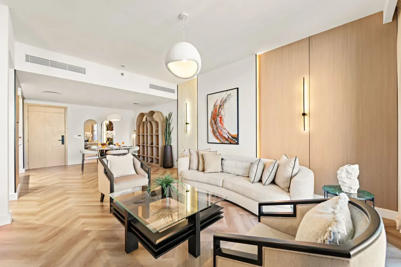 A bright living room with light-colored seating and a glass coffee table.