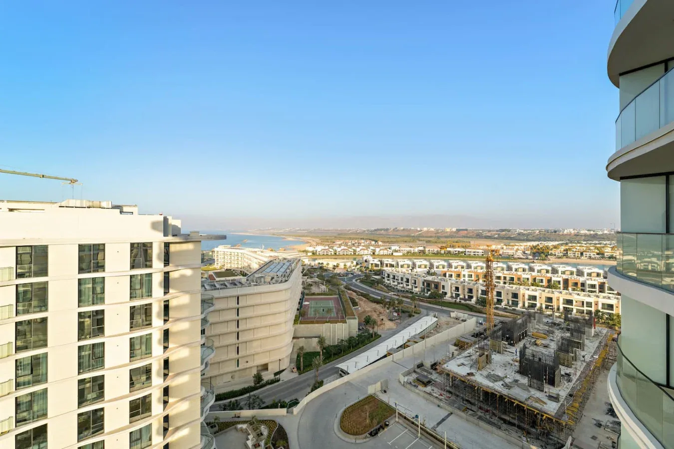 A cityscape viewed from above, with buildings, roads, and construction under a clear sky.