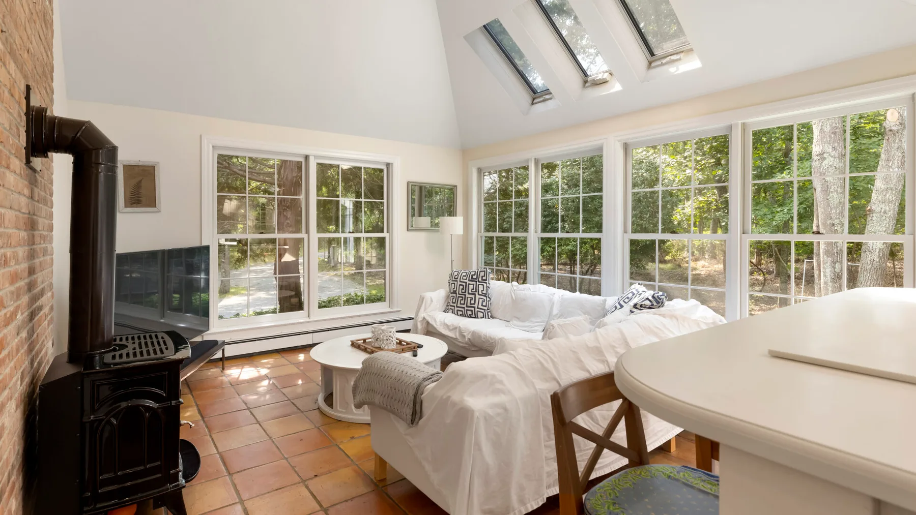 Una sala luminosa con una zona de estar blanca junto a grandes ventanas.