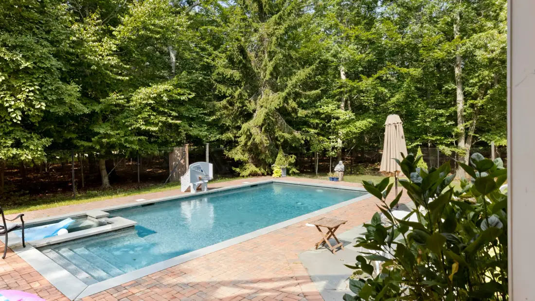 An outdoor swimming pool is surrounded by trees and a paved patio.