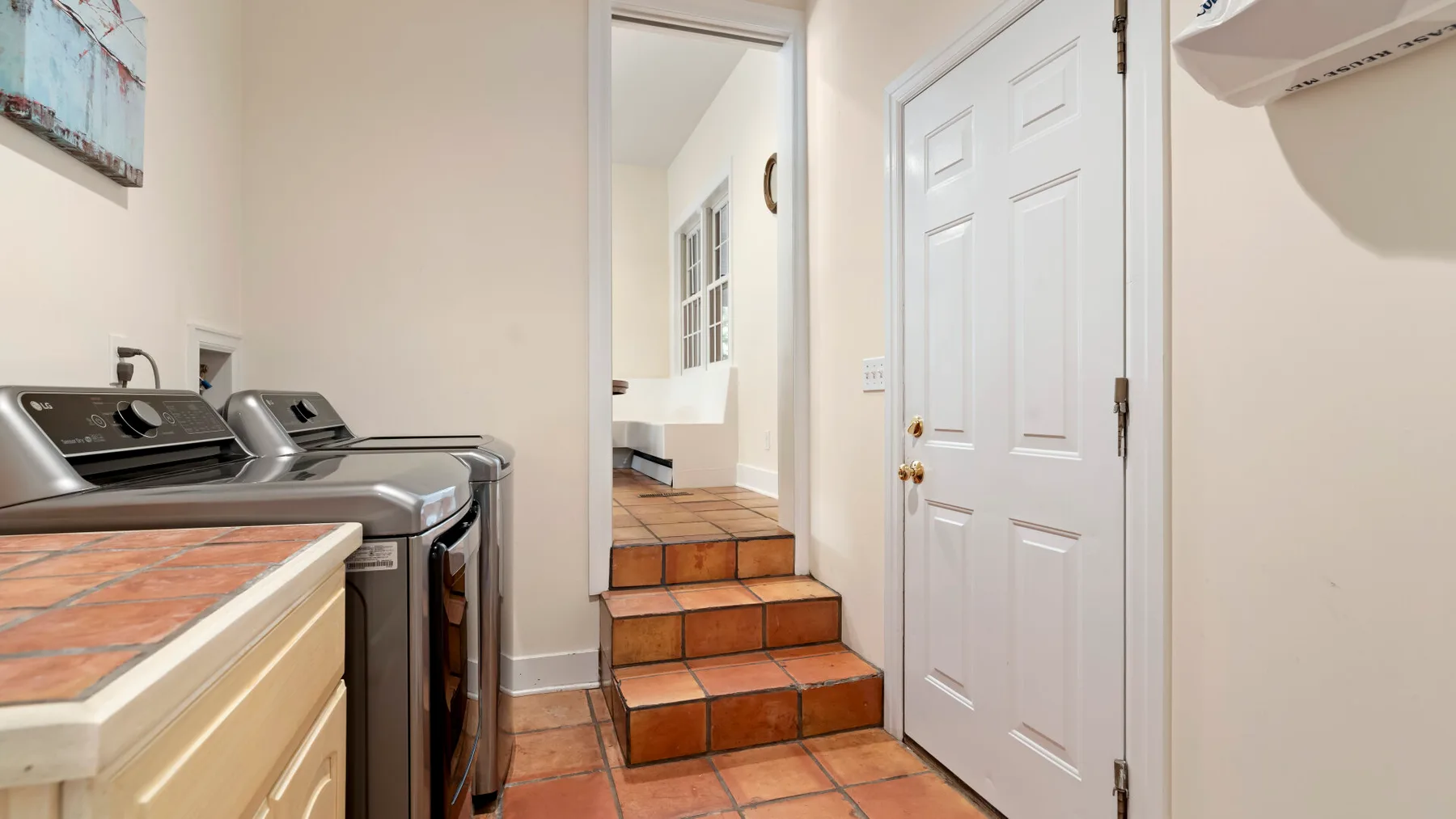 A laundry area beside a doorway, with a washing machine and tiled steps.