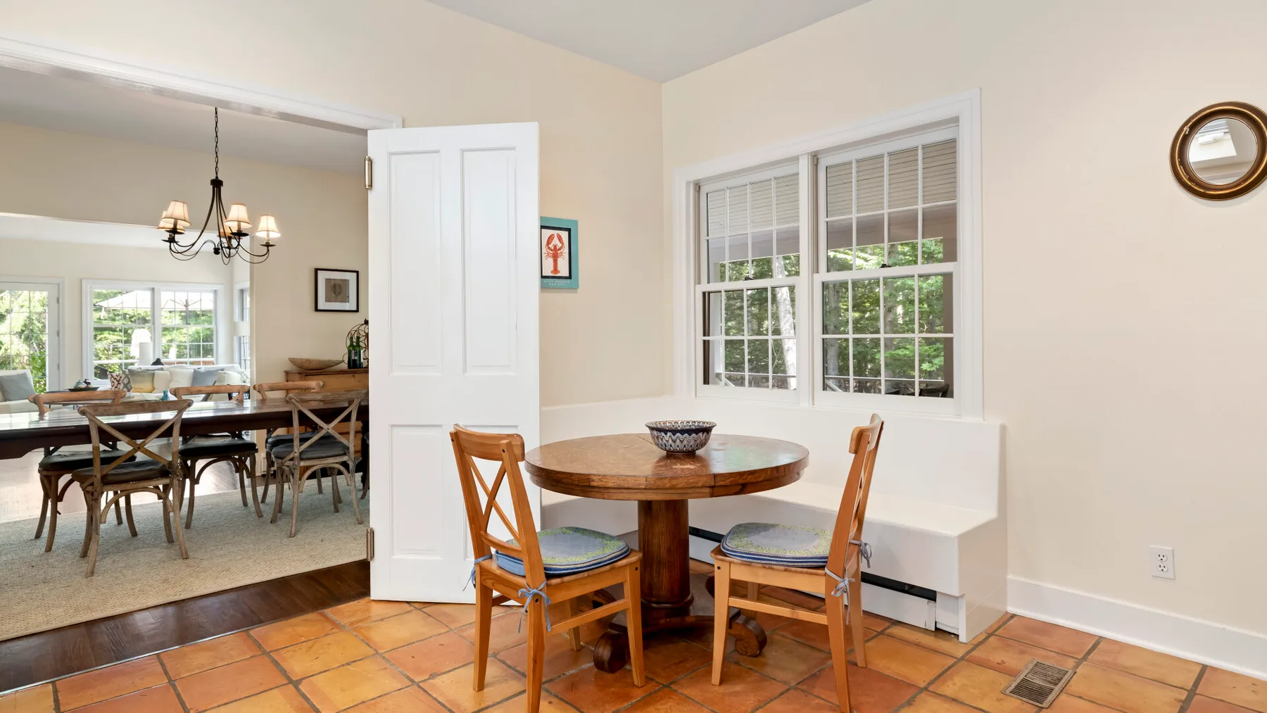 A dining area with a round wooden table and windows overlooking greenery.