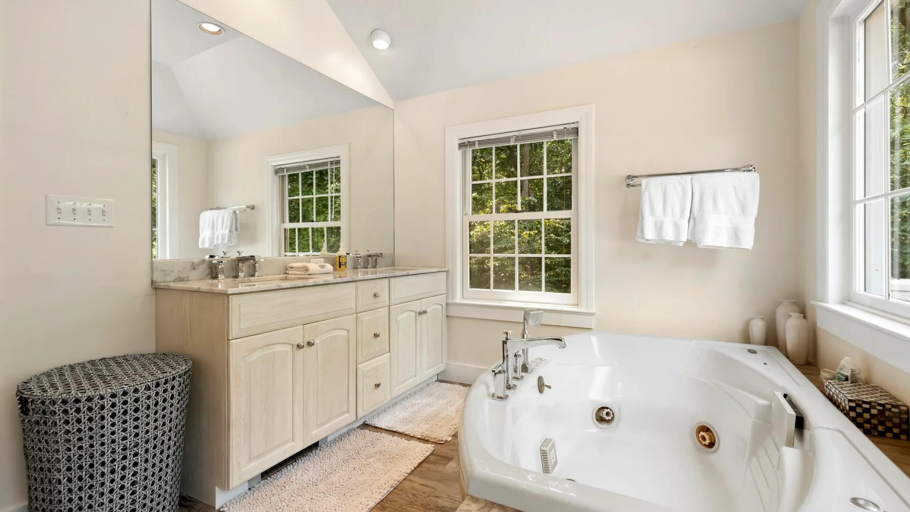 A bright bathroom with a large soaking tub beside a vanity and windows.