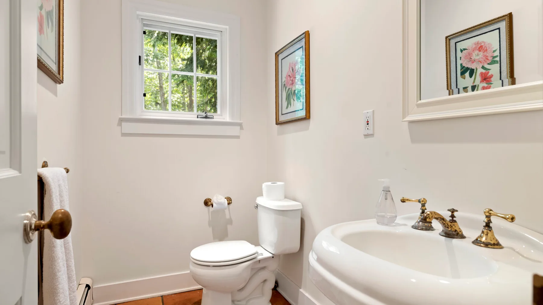 A bathroom with a toilet, sink, and framed floral artwork.
