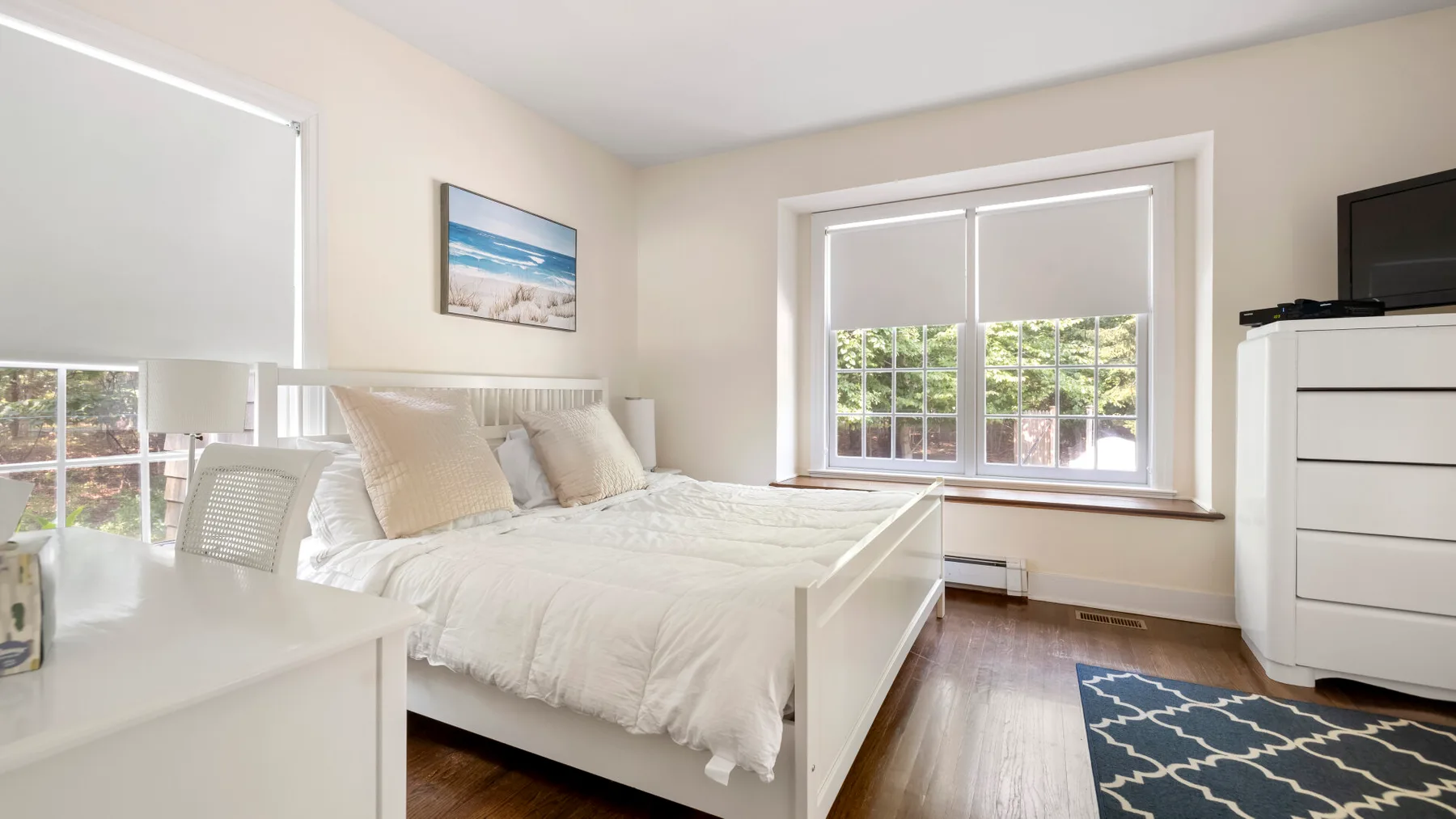 A bright bedroom with a white bed beside a large window.
