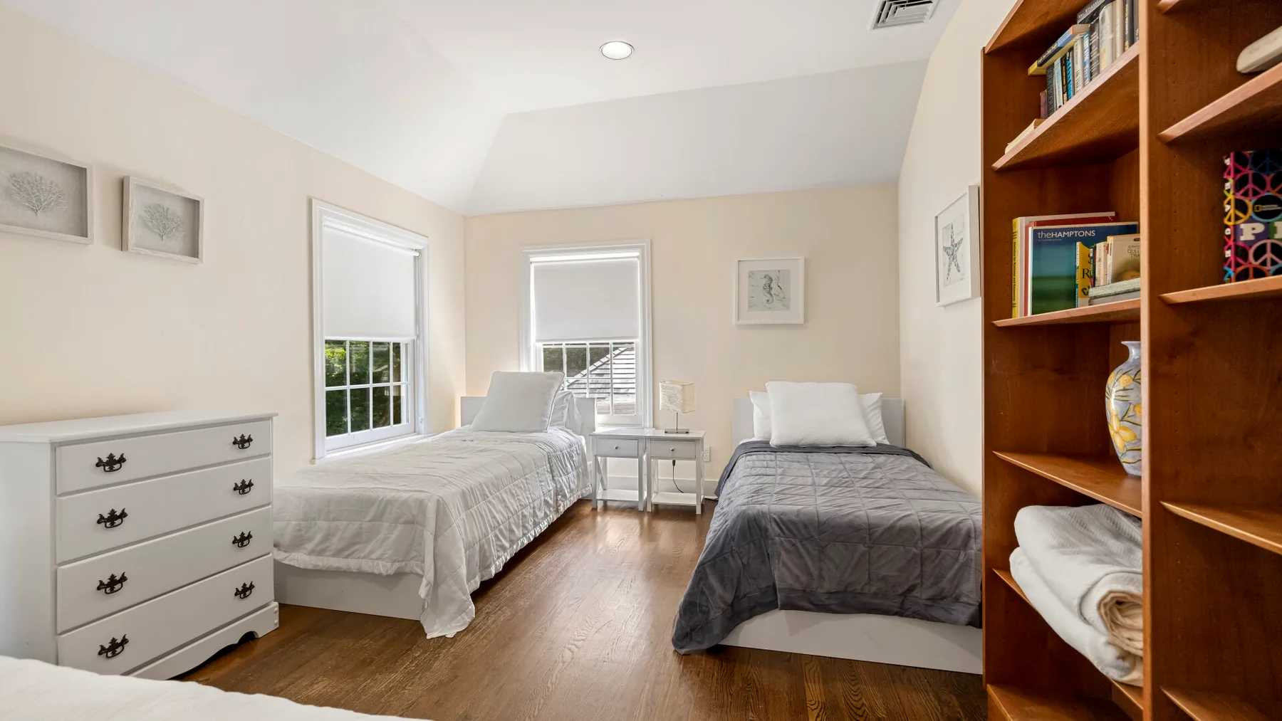 A bedroom with two beds, a dresser, and a tall wooden bookshelf.