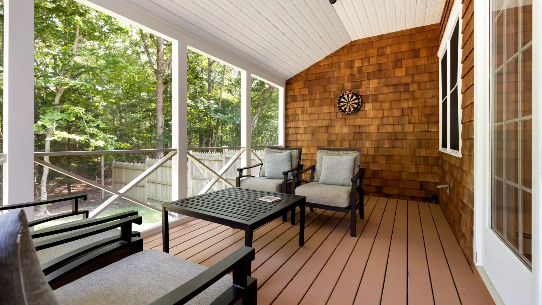 A covered outdoor seating area overlooks leafy trees, with a dartboard on the wood-paneled wall.