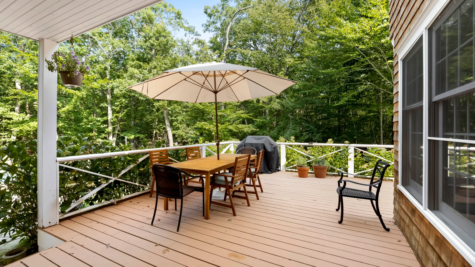 A wooden deck with an outdoor dining table beneath a patio umbrella, surrounded by trees.
