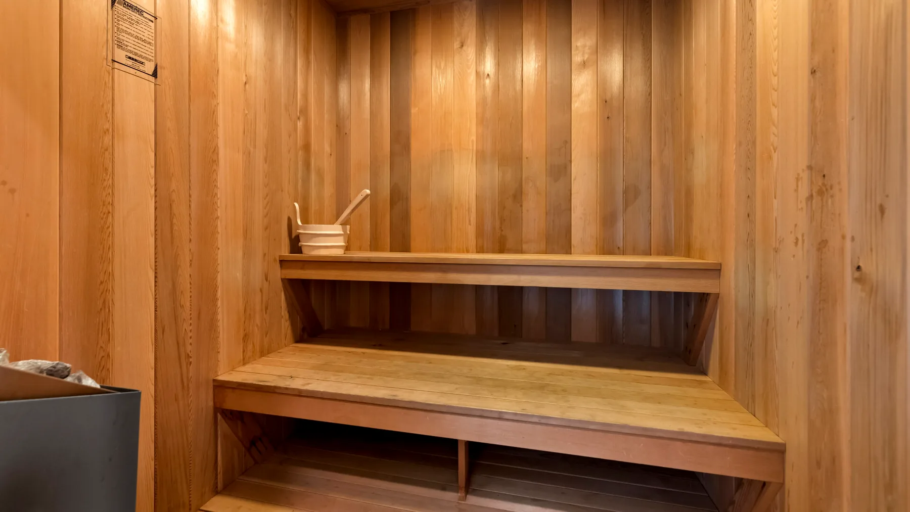 A wood-paneled sauna room with a long bench and a small bucket.