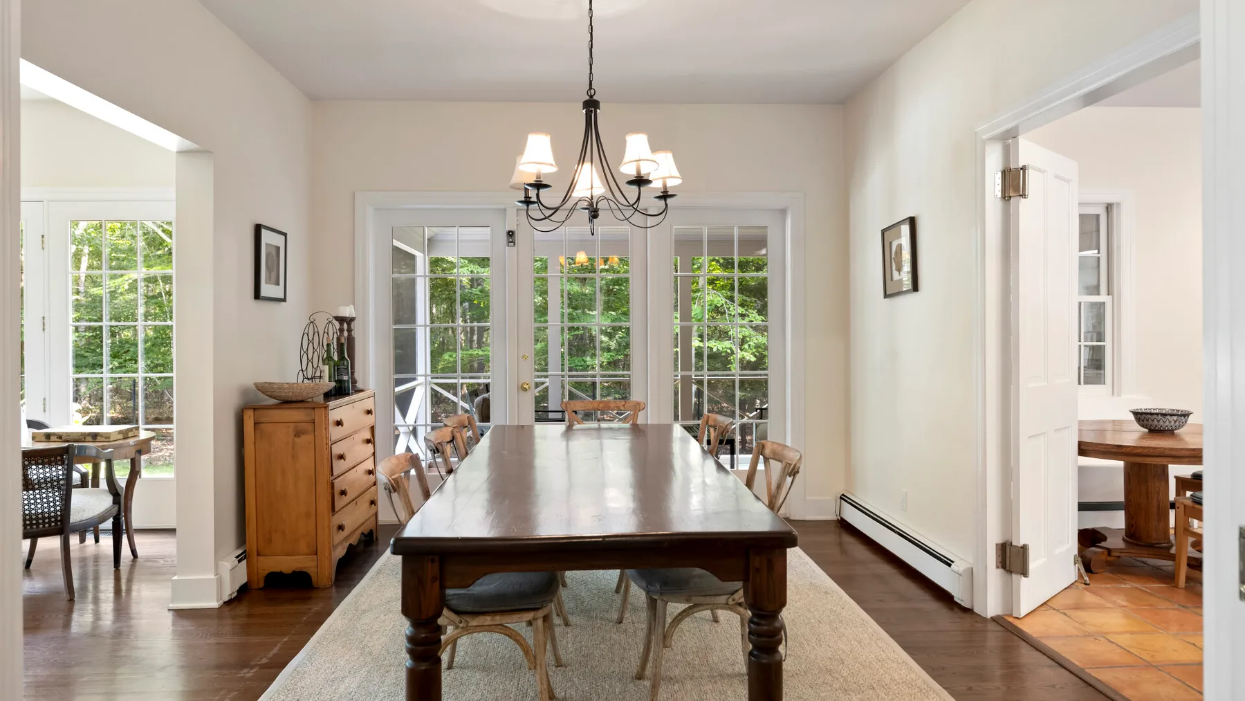 A bright dining room with a long wooden table beneath a chandelier.