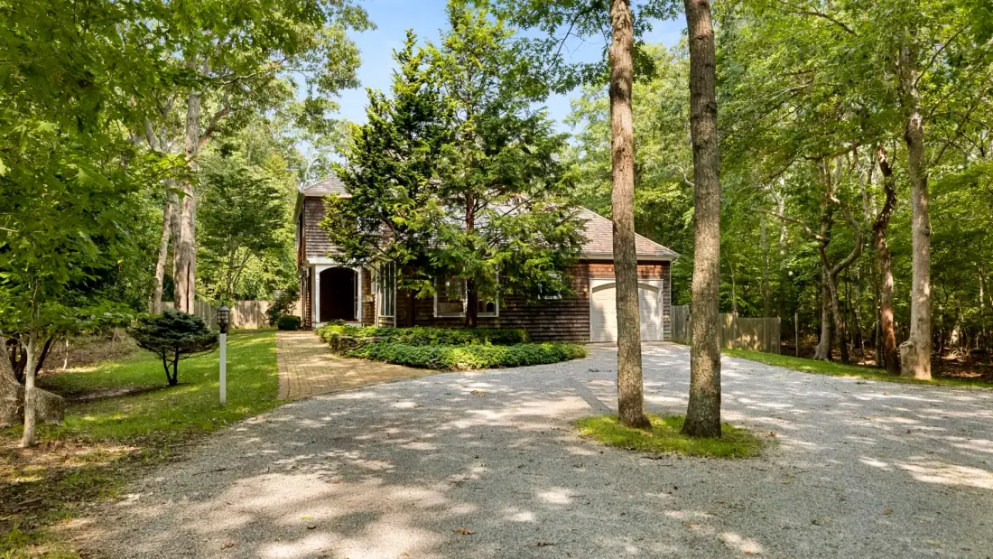 A house stands among trees beside a gravel driveway.