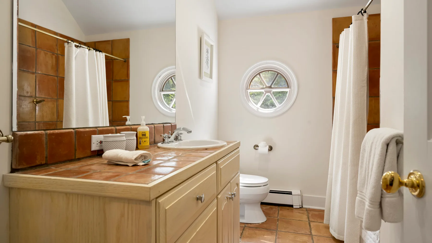 A bathroom with a tiled vanity counter, toilet, and shower curtain.
