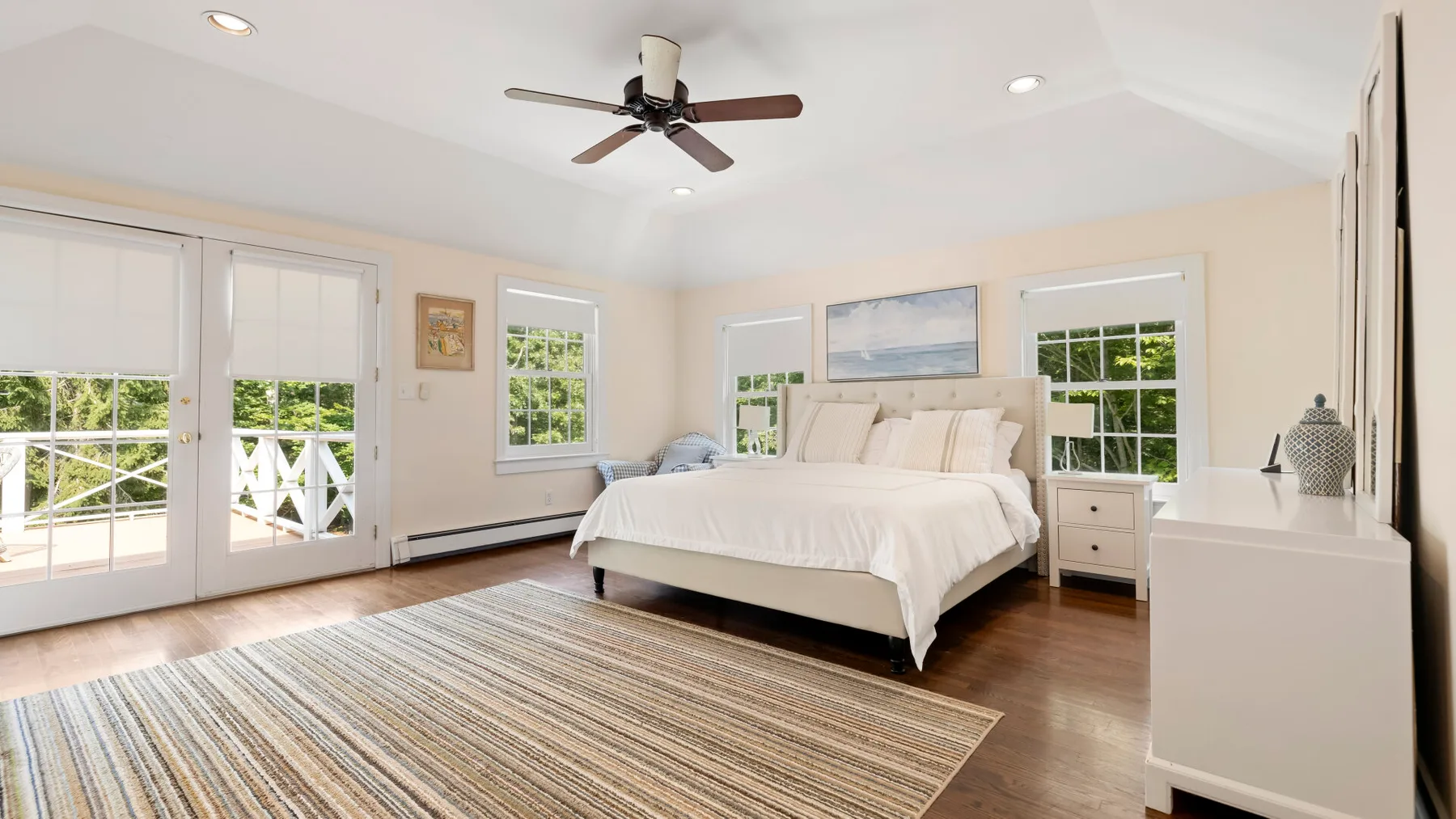 A bright bedroom with a large bed, windows, and a striped rug.