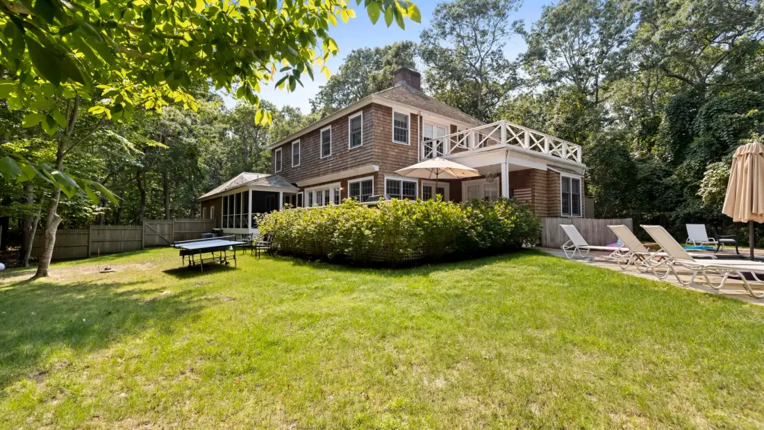 A two-story house overlooks a broad grassy yard with outdoor seating.