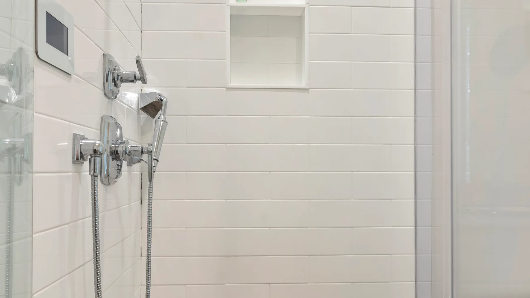 A tiled bathroom shower with chrome fixtures and a recessed wall niche.