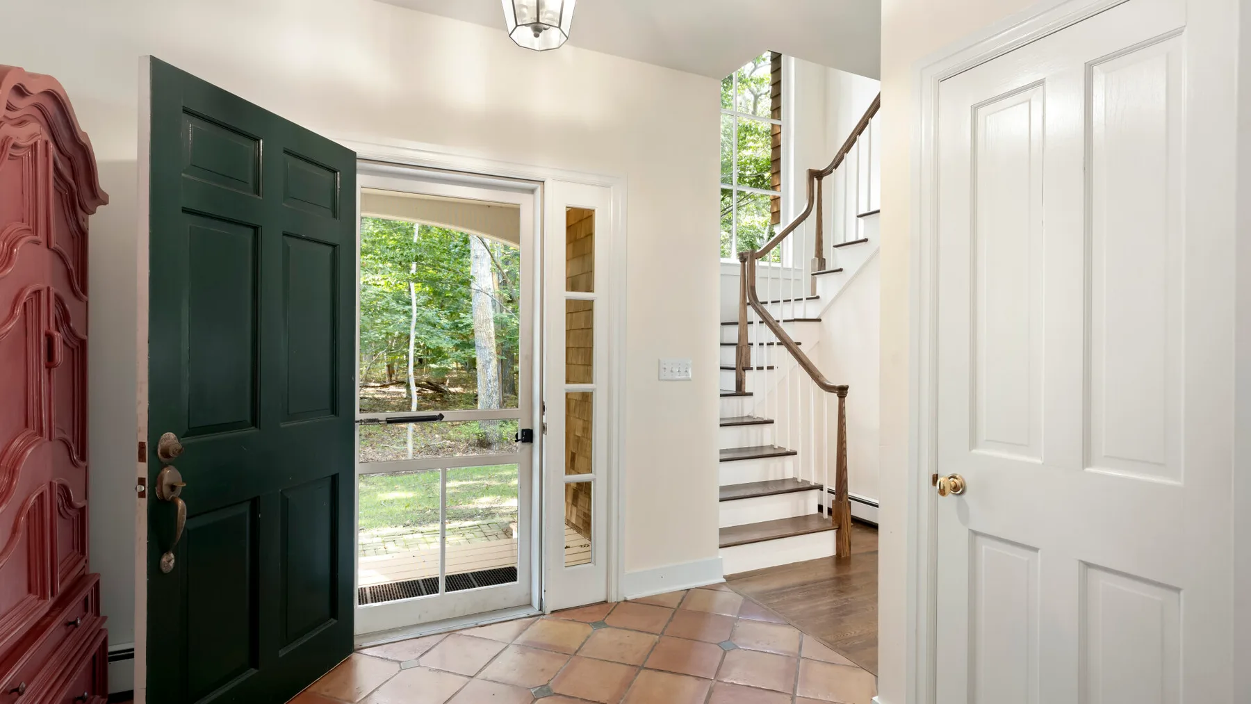 An entryway with a dark green door, tiled floor, and staircase.