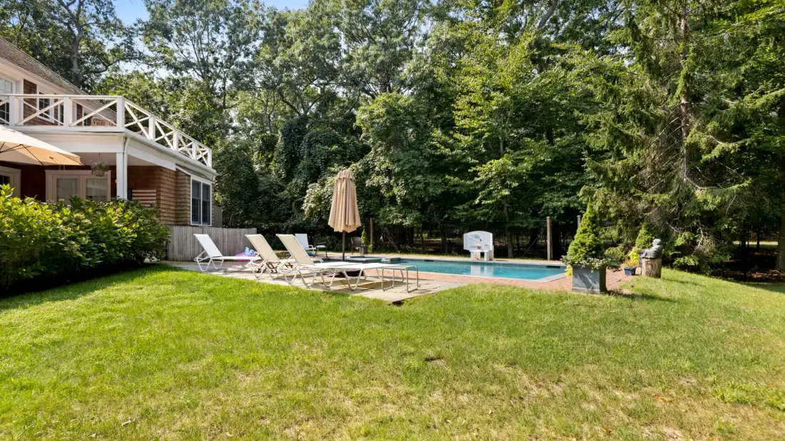 A backyard pool beside a lawn, with lounge seating and trees around it.