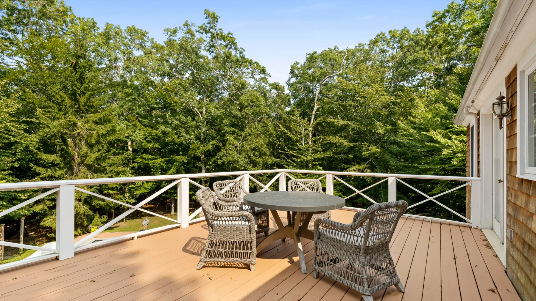 An outdoor deck with a table and seating overlooks a wooded area.