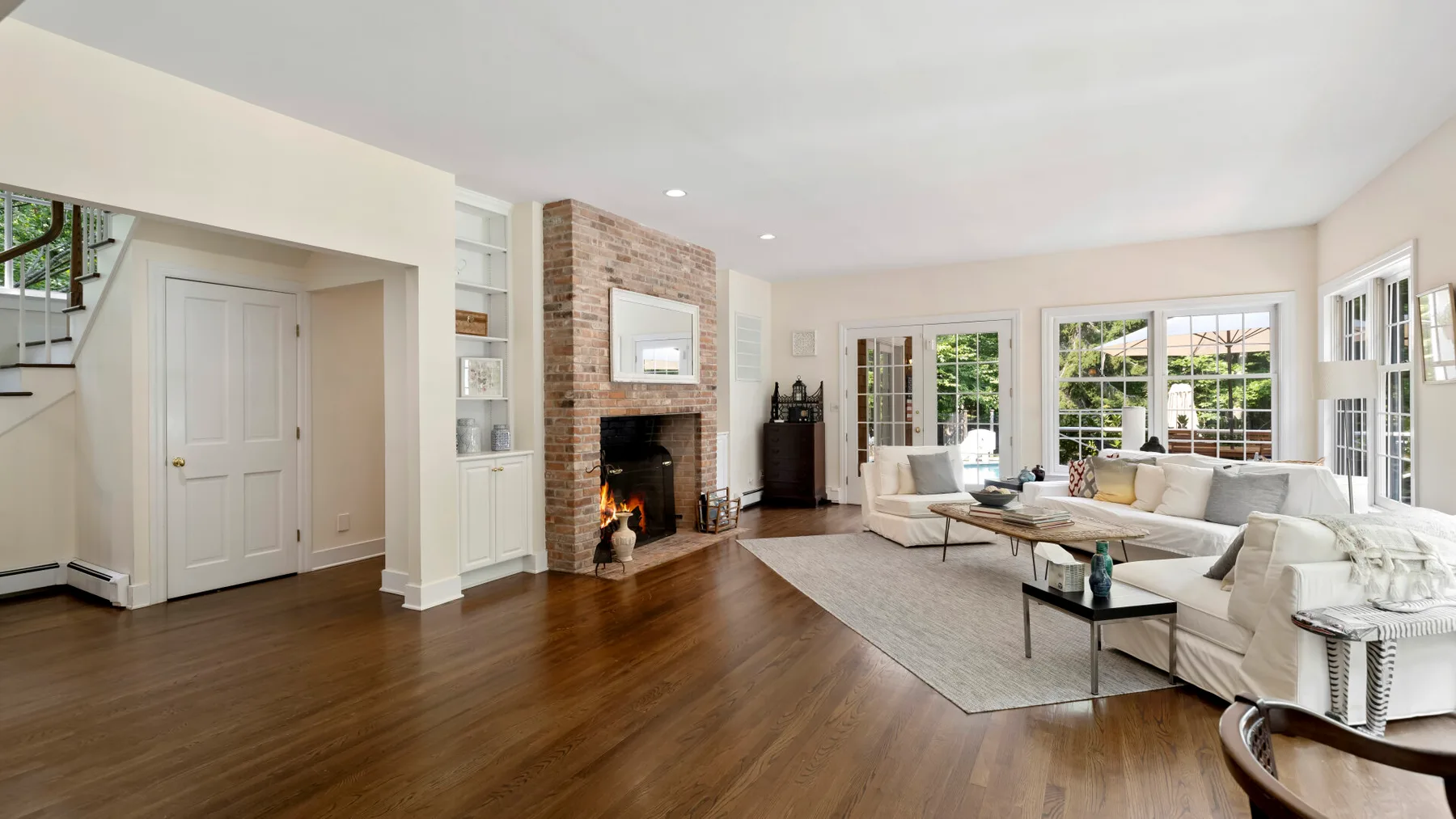 A bright living room has light-colored seating arranged around a fireplace.