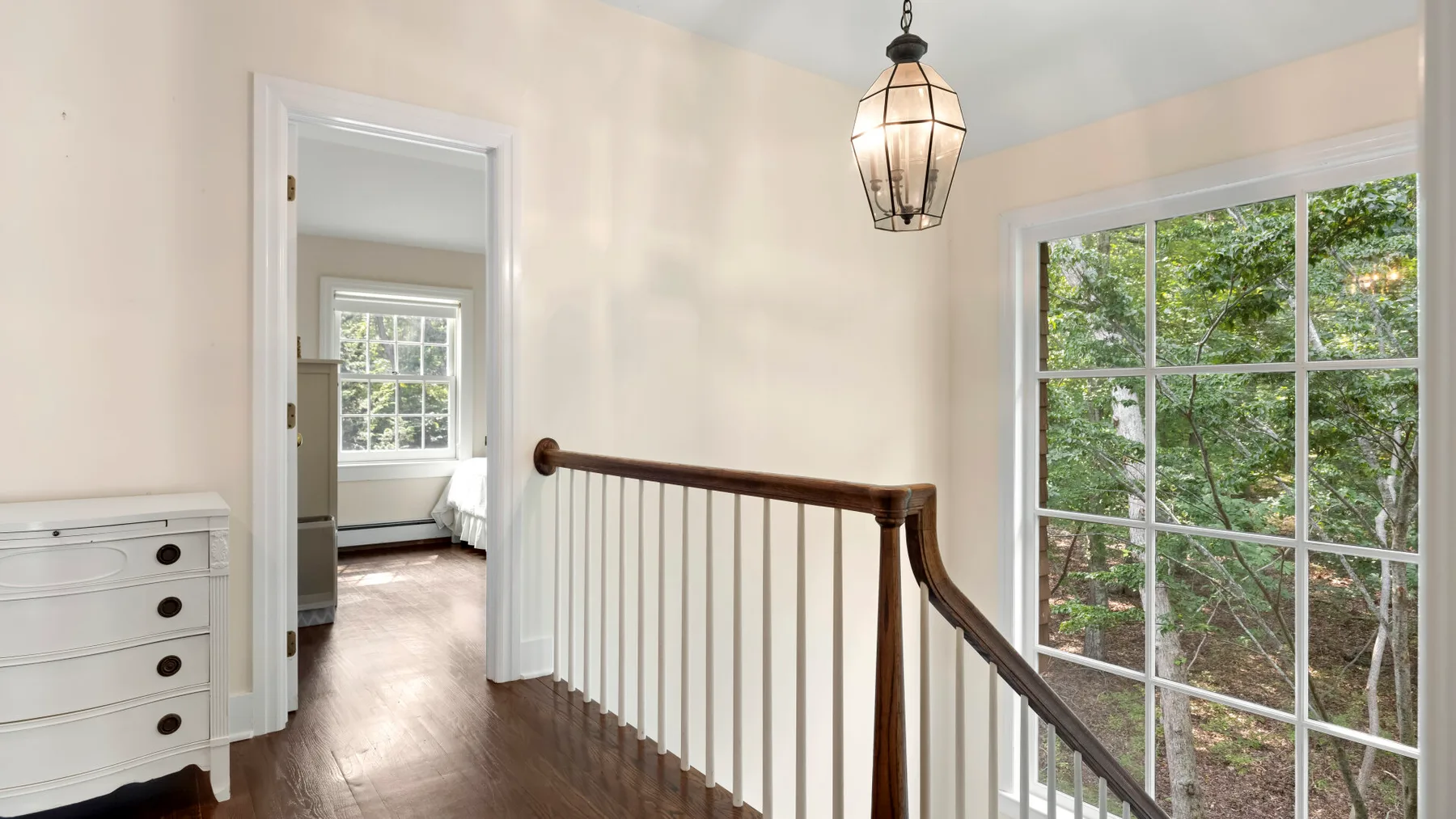 A bright upstairs landing has a wooden railing and large windows overlooking greenery.