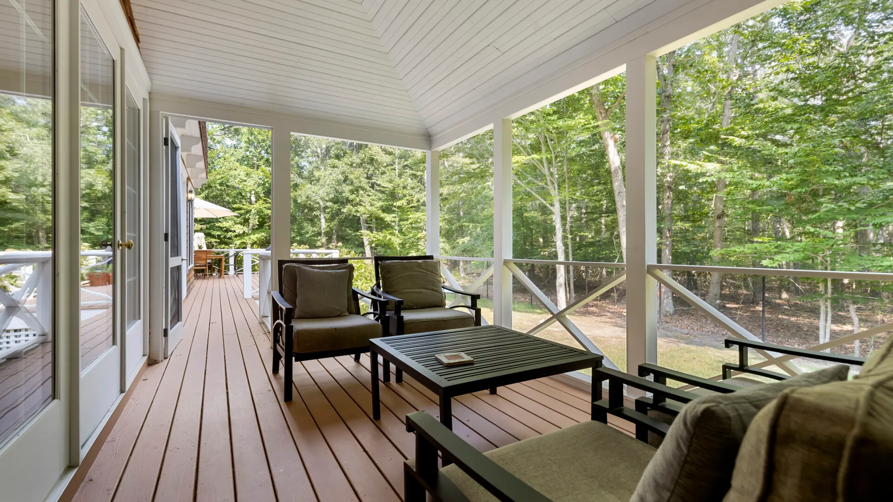A covered outdoor seating area with a low table overlooks a wooded yard.