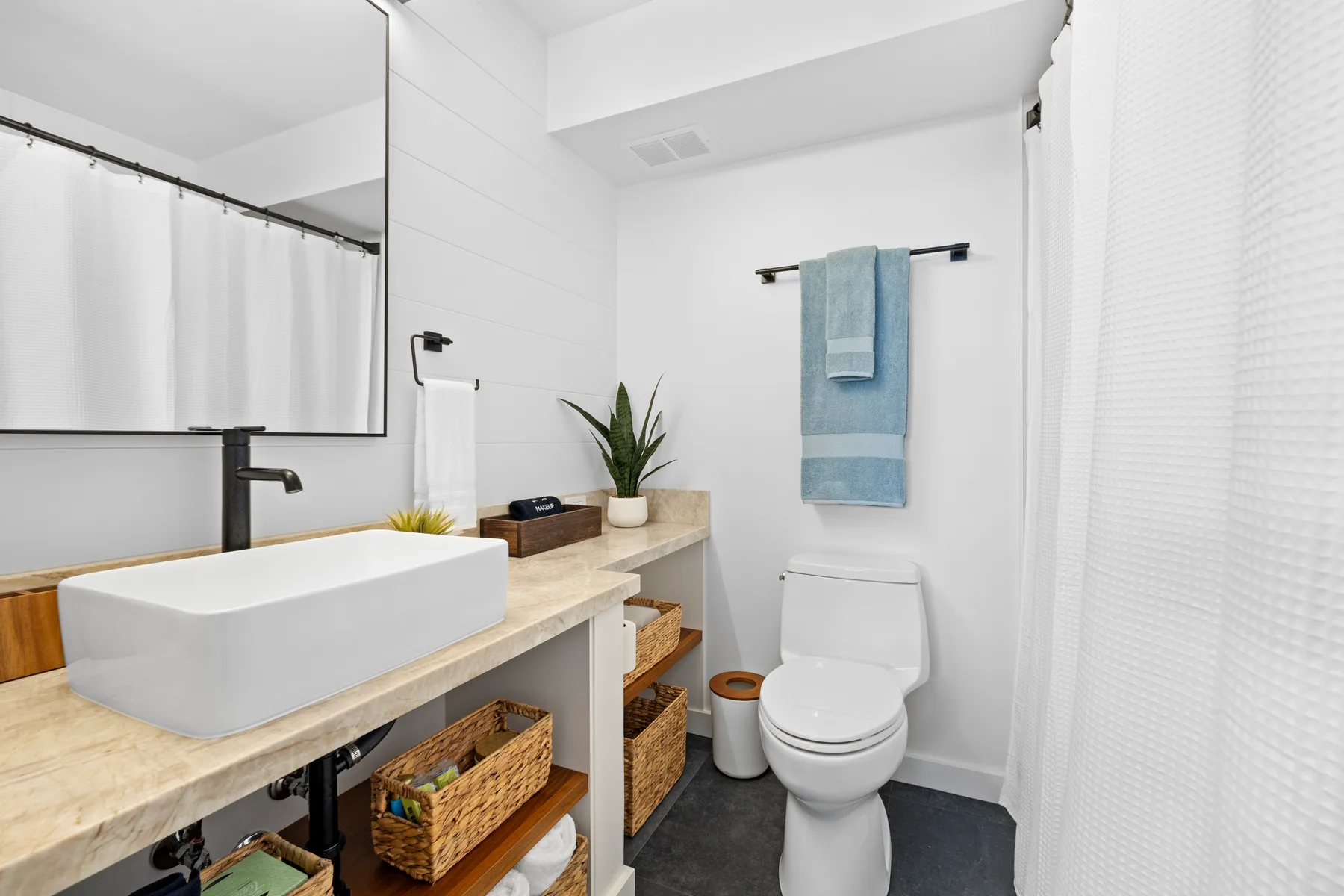 Un baño luminoso con lavabo sobre encimera, inodoro y toalla azul.