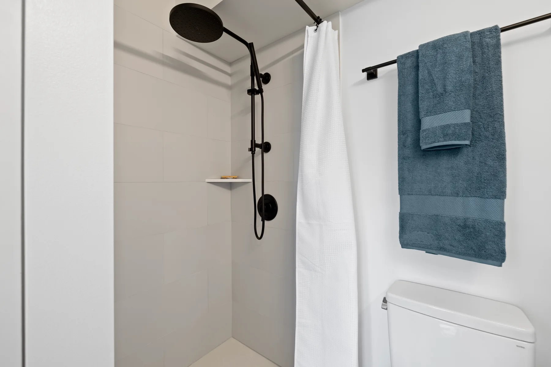 Una ducha de baño con una cortina blanca y toallas azules colgadas cerca.