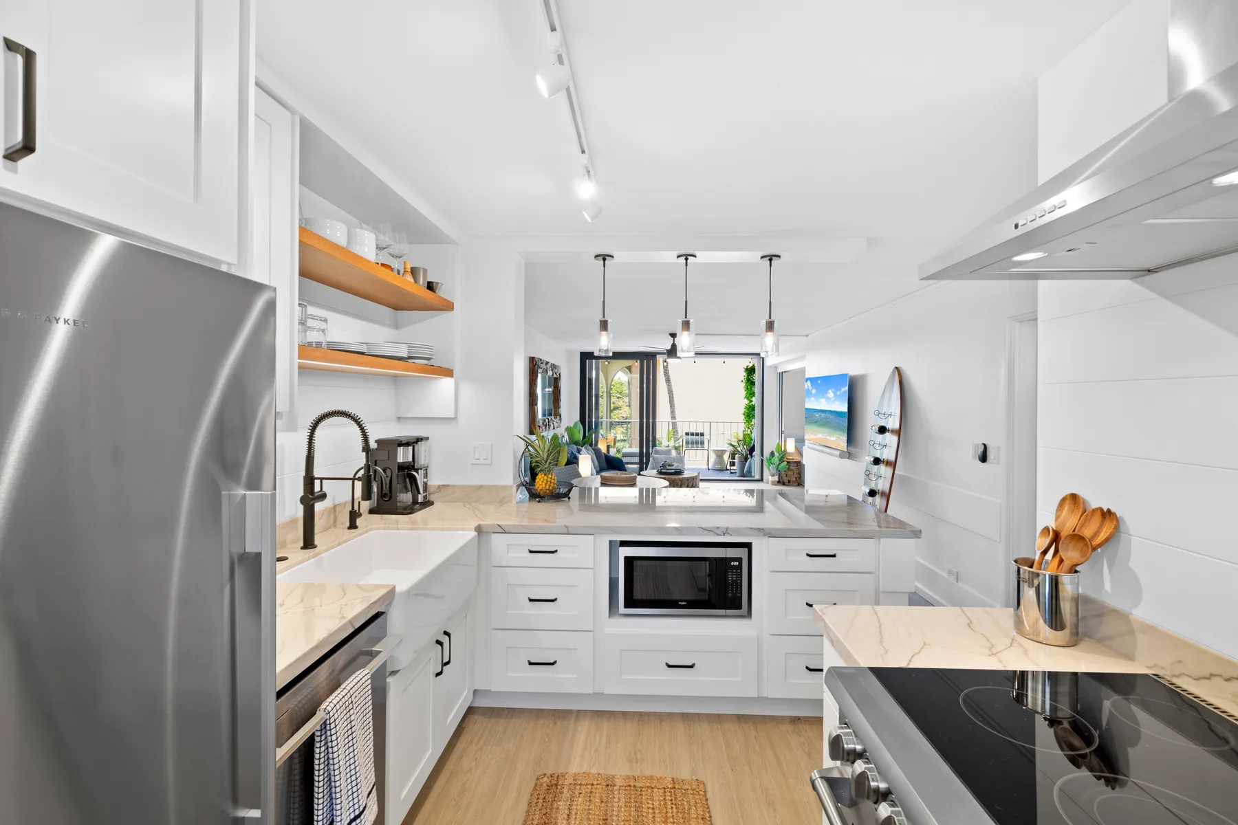 Una cocina blanca y luminosa con isla, placa de cocción y electrodomésticos de acero inoxidable.