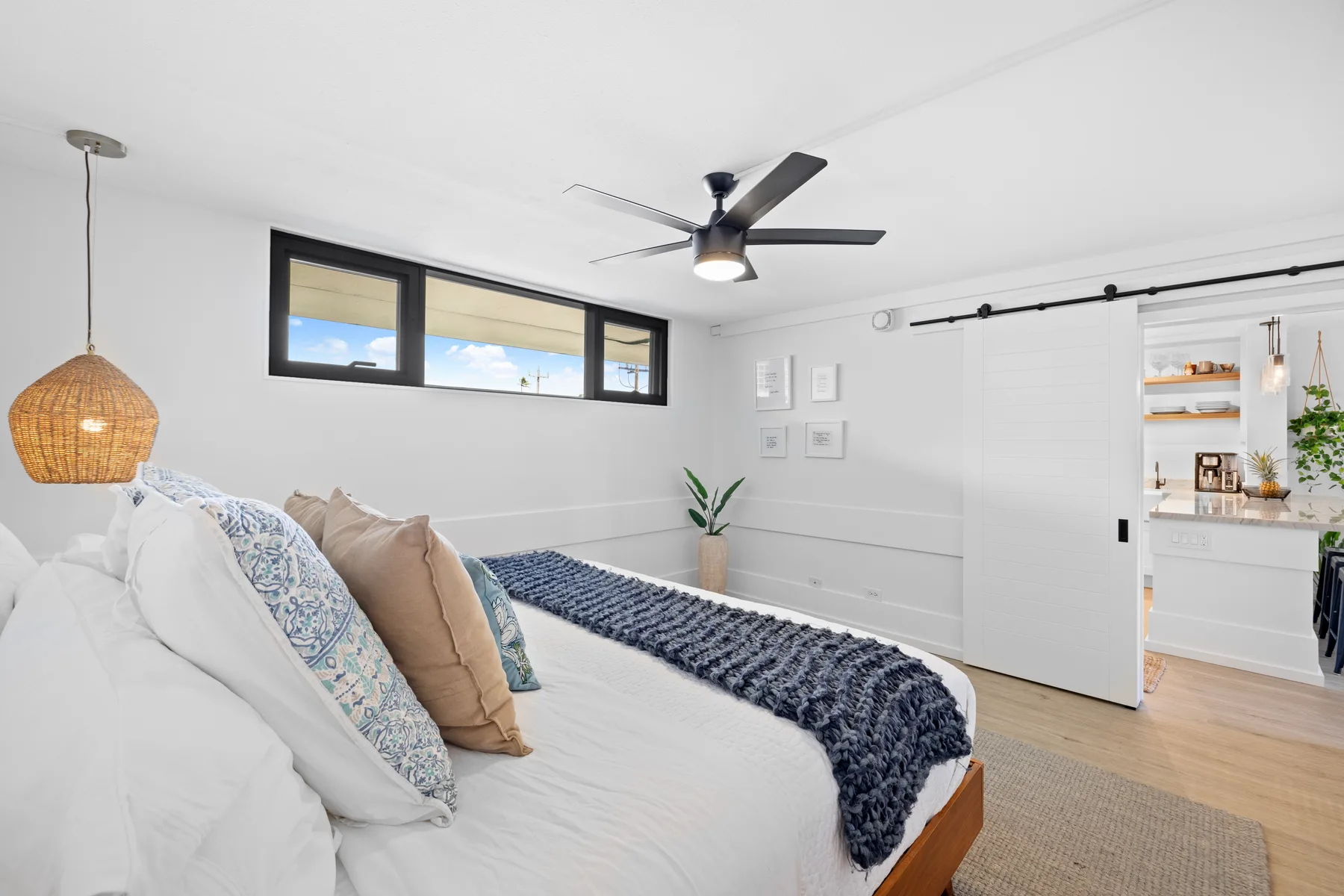 Un dormitorio luminoso con una cama, ventanas altas y un ventilador de techo.