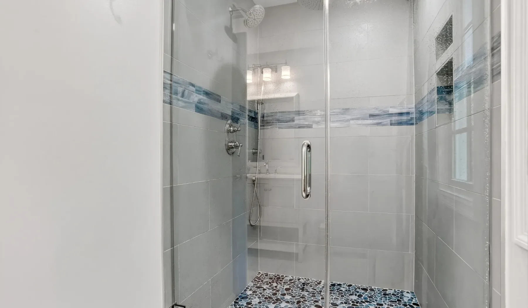 A tiled bathroom shower with glass panels and a blue patterned band.