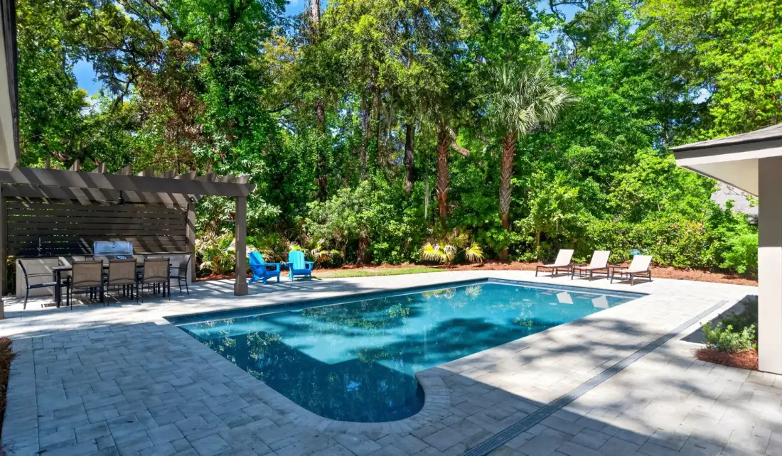 A swimming pool sits beside a paved patio and shaded outdoor seating area.