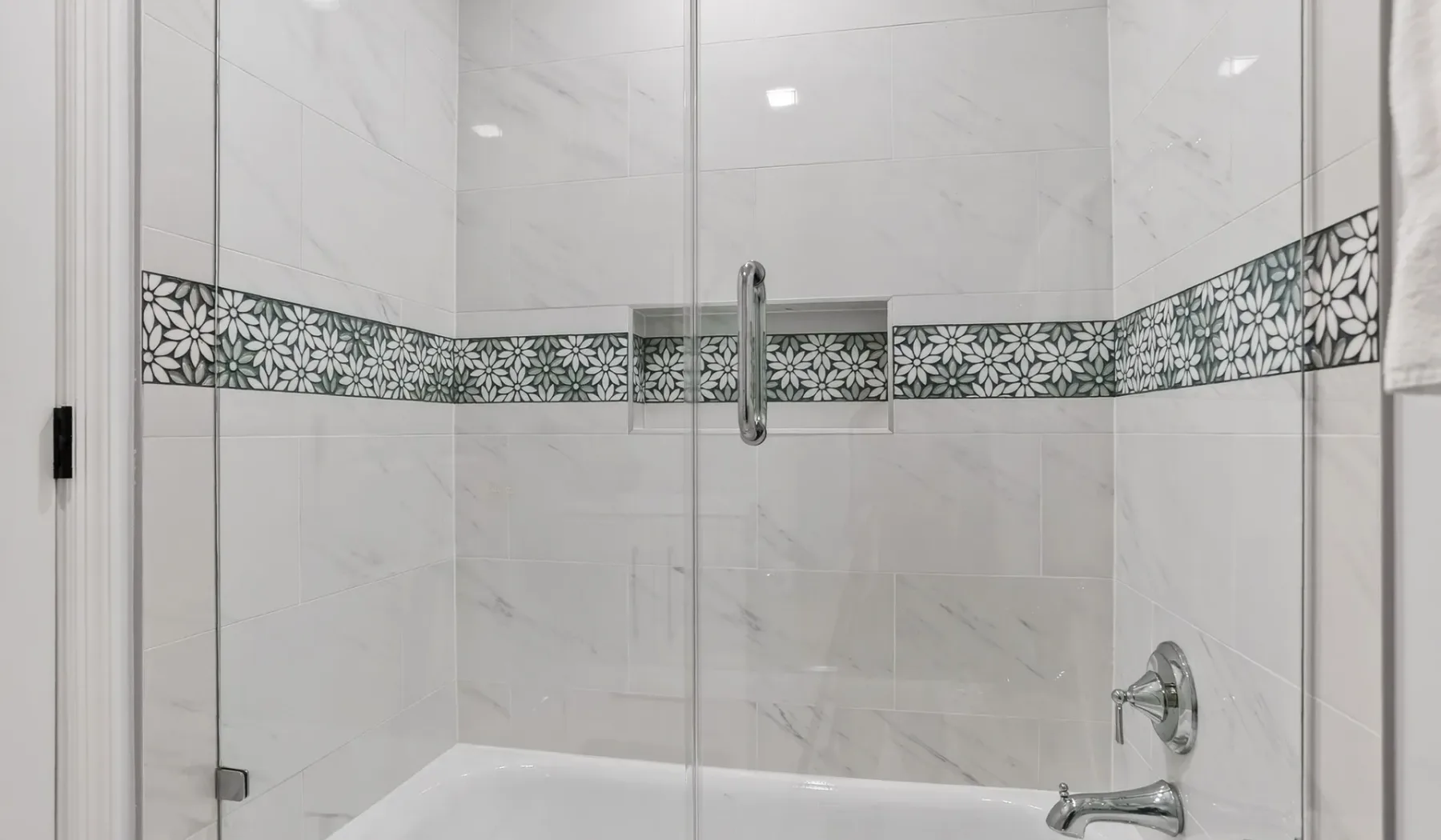 A tiled bathroom shower with a decorative patterned band across the walls.