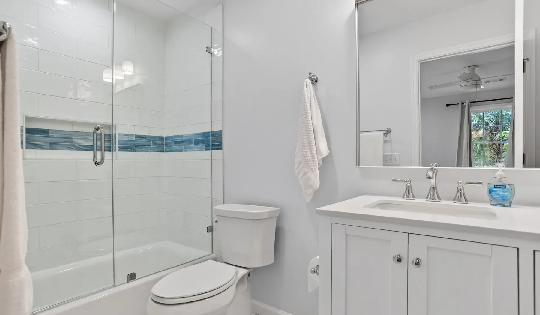 A bright bathroom with a glass shower, toilet, and sink vanity.