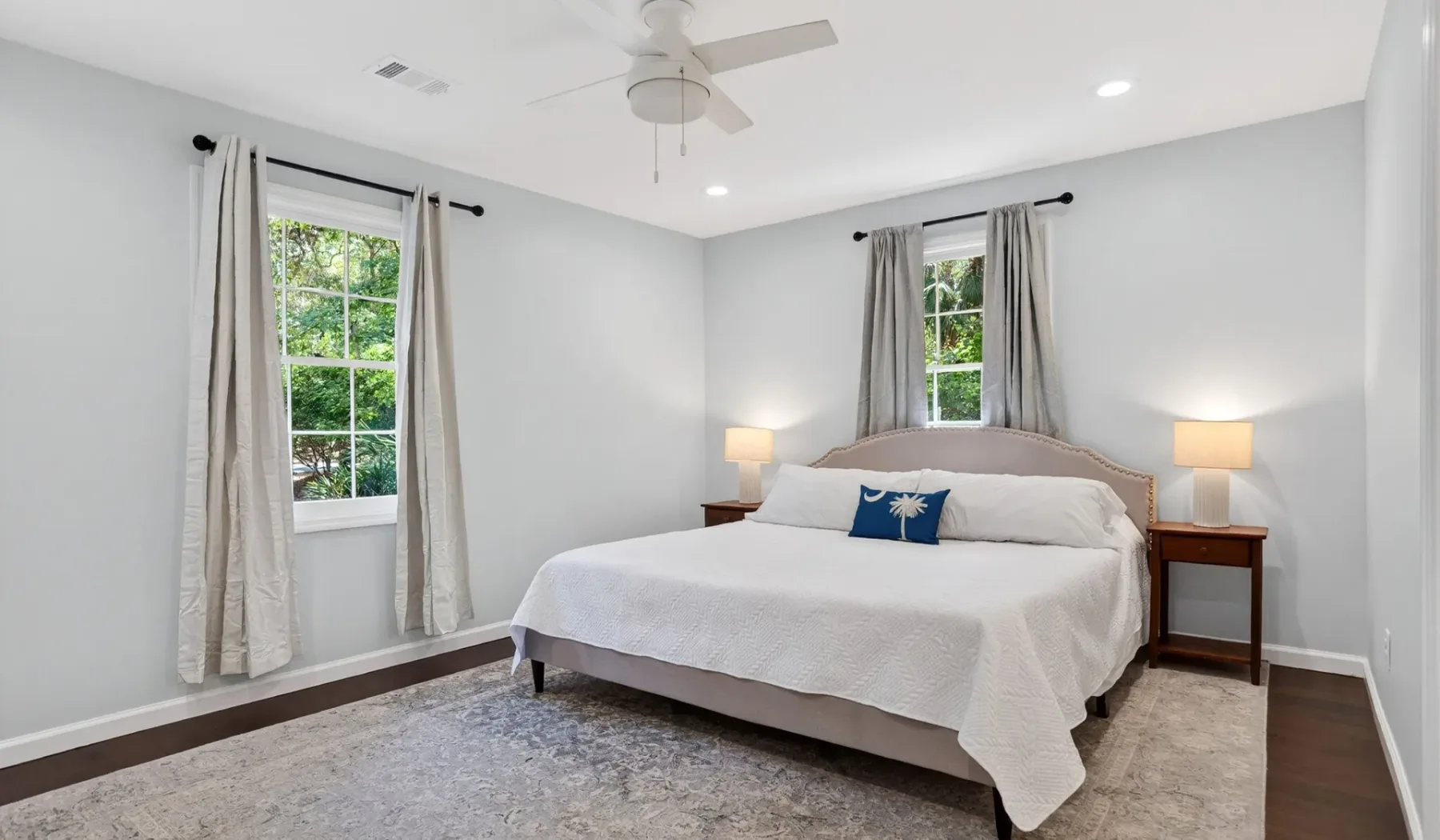 A bedroom with a neatly made bed and two windows with curtains.