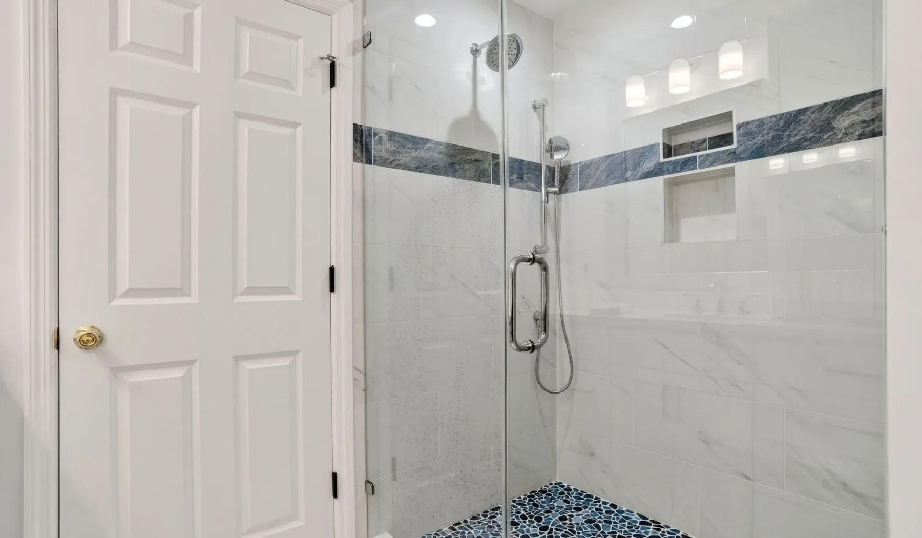 A bright bathroom with a glass shower and dark tile accents.