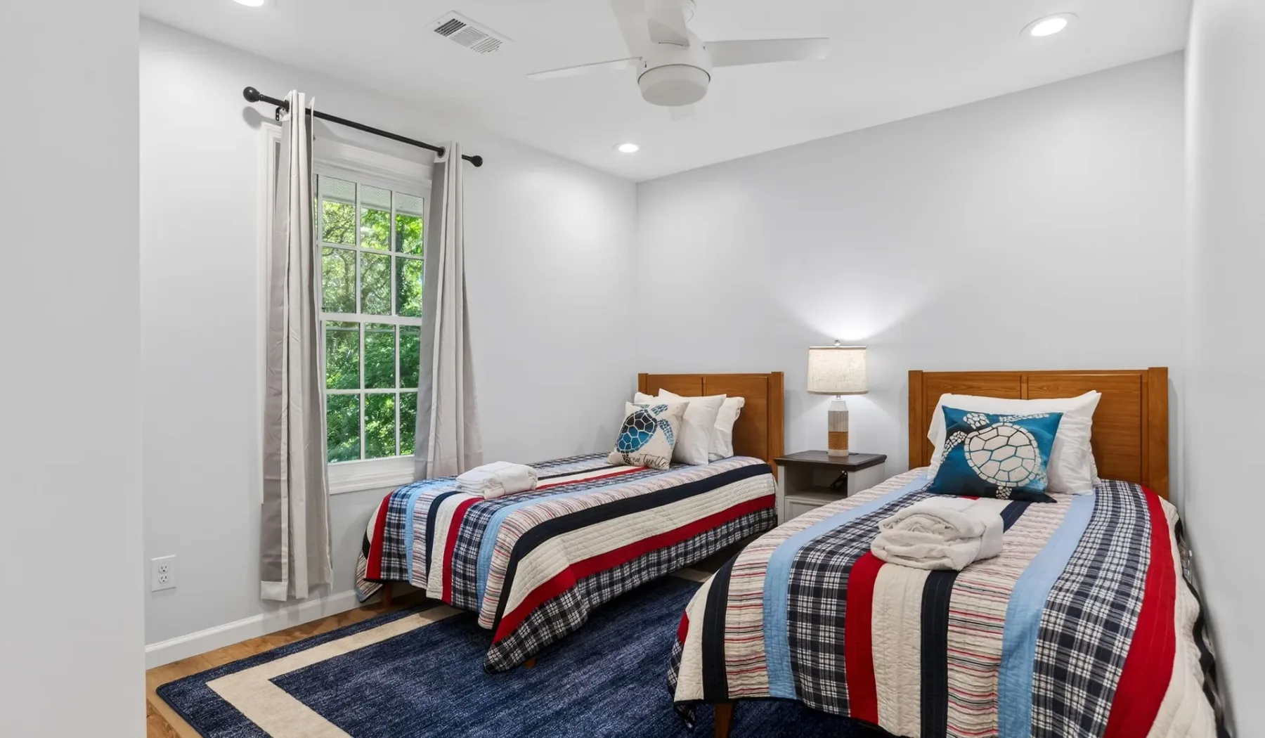 A bright bedroom with two beds, striped bedding, and a window.